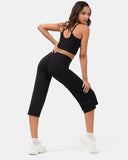 Woman wearing a black sports bra and high-waisted black cropped activewear pants with white sneakers.