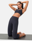 Woman wearing a navy blue sports bra and high-waisted yoga pants kneeling on a gray mat.