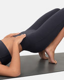 Woman in a black sports bra and high waisted black leggings practicing yoga on a mat.