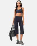 Woman wearing a navy blue sports bra and high-waisted cropped leggings with a gym bag.